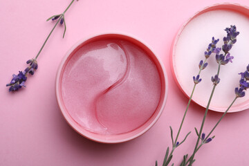 Package of under eye patches and lavender flowers on pink background, flat lay. Cosmetic product