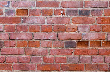 Close-up background of ancient red brick wall shabby aged with grains of stone dips and scuffs