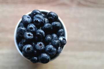 Cup of fresh blueberries on wooden table. Flat lay.