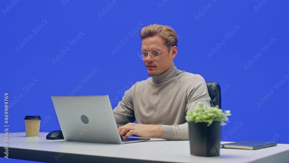Poster modern office green screen background: businessman sitting at his desk working on a laptop computer.