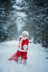 Fototapeta na wymiar Little funny child dressed in Santa Claus red costume bringing presents in winter snowy forest. Christmas Eve.