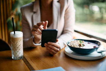 Close-up of businesswoman uses smartphone during her breakfast in cafe.