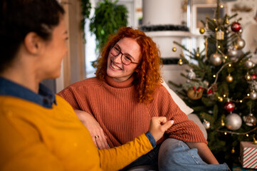 Two beautiful friends exchanging christmas gifts in the apartment smiling and laughing in front of...