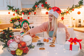 Family of mother and daughter make homemade gingerbread for christmas at decorated kitchen at home. Christmas atmosphere, preparing