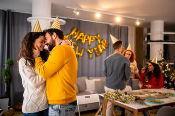 Young beautiful couple cuddling and kissing on a new year's eve party in their apartment, celebrating with friend and family having a nice dinner.