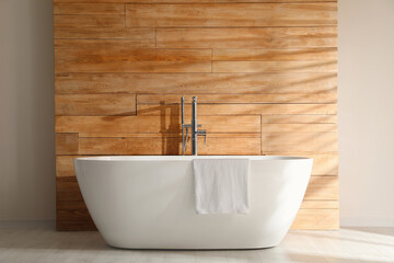 White bathtub with towel near wooden wall in room