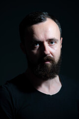 dramatic portrait of bearded millennial on black background