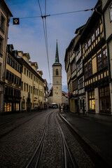 Fototapeta na wymiar Street with a rail and a church at the background in a dark mood. Erfurt, Germany 