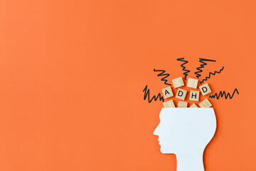 Silhouette of human head with chaotic lines and wooden blocks with the letters ADHD on orange background. Minimal concept of attention deficit hyperactivity syndrome. Copy space - obrazy, fototapety, plakaty