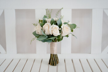 wedding bridal bouquet of white roses stands on a white wooden bench, close-up of the bouquet on a light background
