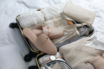 Open suitcase with folded clothes, shoes and accessories on bed
