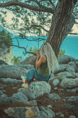 Rasta girl with dreadlocks is resting on the Mediterranean coast on a swing