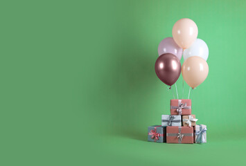 Bunch of color balloons and beautifully wrapped gift boxes on green background. Space for text