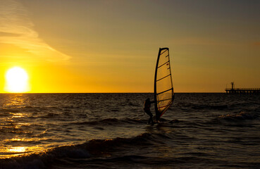 Sap board with a sail on the background of an orange sunset. Sea with waves. Surfer silhouette....