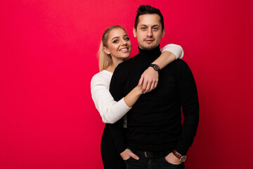 Photo of a beautiful pretty positive smiling happy young blonde woman with makeup and ponytail in a stylish white knitted sweater and black pants and an adult brunet man with stubble in a black