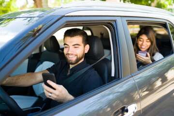 Handsome male driver and female passenger smiling while looking at the ride share app on the smart phone