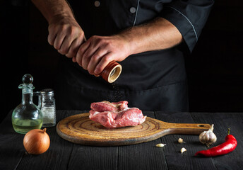 Professional chef cooking raw meat fillet and adding pepper or chili for marinade. Working environment in kitchen restaurant or cafe.