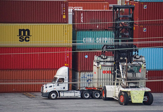 Los Angeles, California USA - November 16, 2021: A specialized fork lift removes a shipping container from a truck to stack it in a freight terminal, Port of Los Angeles.