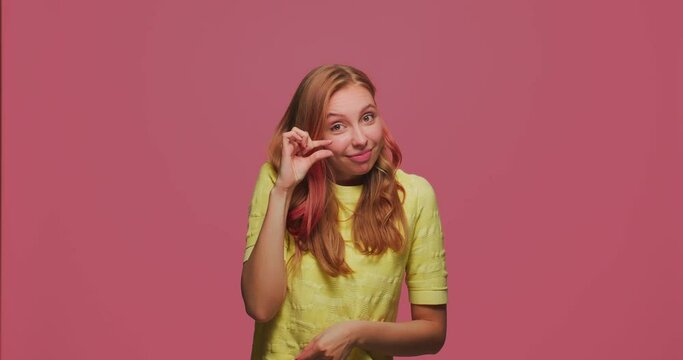 Little bit gesture. Funny happy young girl showing small size by fingers, winking ask little more, body language concept