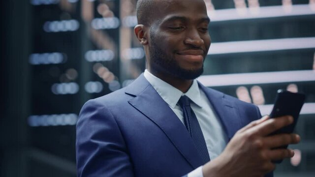 Portrait of Successful African-American Businessman on the Street of the Central Business District in Big City. Black Digital Entrepreneur uses Mobile Phone e-Commerce App for Stock Market Investment