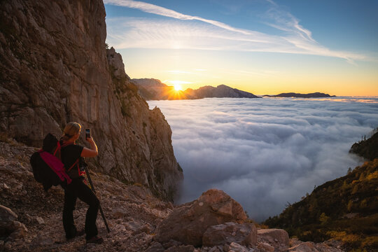 Woman photographing sunrise in mountains looking at foggy valley.