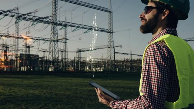 Electric engineer wearing helmet safety vest working with tablet near high voltage lines power station holographic energy animation during sunset shot in 4k super slow motion