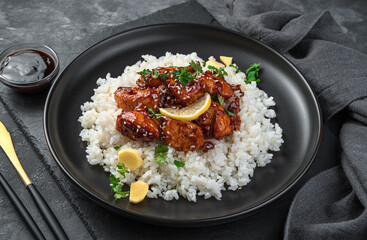 Teriyaki chicken with rice, sesame seeds and fresh parsley on a dark background.