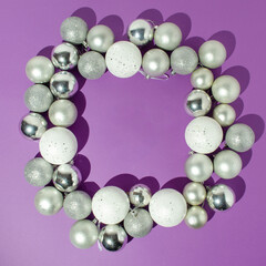 White, shiny and silver Christmas balls composition on a purple background with empty space in the middle. New Year card idea.