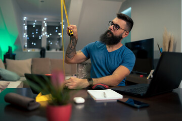 Young businessman working at home while using laptop and tape measure