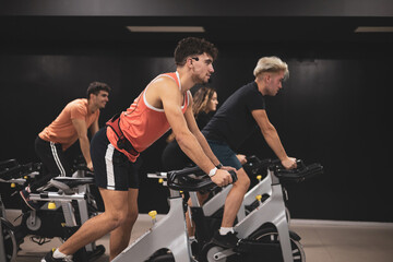 4 young people giving an exercise bike class in a gym. - obrazy, fototapety, plakaty