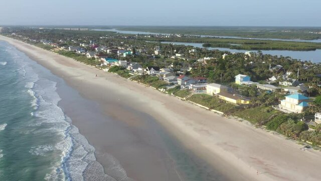 Aerial tilt-down of Florida east coast barrier island beachfront community Wilbur By The Sea: beach, ocean surf, residential houses, sea walls, Halifax river,  and Atlantic Intracoastal Waterway.