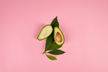 Fresh beautiful green avocado and leaves on a pink background. Beauty, health, aesthetics.