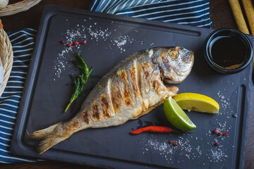 Grilled fish on a plate with a glass of wine and baked vegetables.