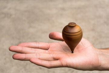 Close up of a traditional spinning top made out of wood balancing on a man's hand. Blurred concrete...
