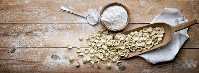 Wholemeal Apulian orecchiette. Orecchiette pugliesi in scoop with whole durum wheat semolina on rustic wooden background, top view, space for text.