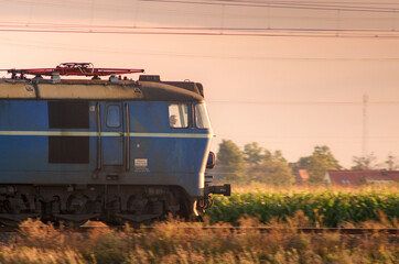 Polska elektryczna lokomotywa towarowa jadąca wczesnym wieczorem w stronę zachodzącego Słońca.