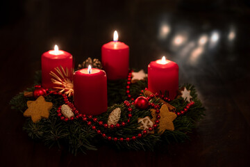 Obraz na płótnie Canvas Decorated advent wreath from fir branches with red lit candles, Christmas balls and star cookies, some blurred lights in the dark background, copy space, selected focus