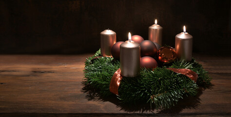 Third Advent wreath with copper colored candles and Christmas decoration baubles on a rustic wooden...