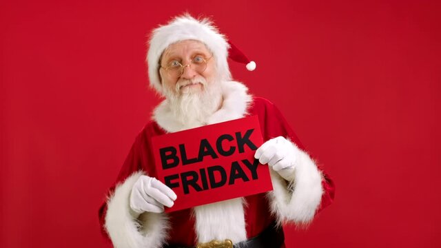 Happy Santa Claus is Dancing Merrily Holding mock up Banner With Inscription BLACK FRIDAY. Santa Claus is Enjoying Big Discount Sale on Black Friday Dancing on Red Background. Christmas sales.
