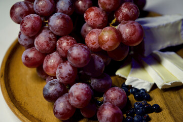 Grapes, blueberries and cheese on a wooden plate