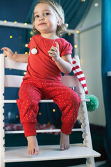 Kid girl red pajamas decorating room Christmas. Winter holidays, new year eve