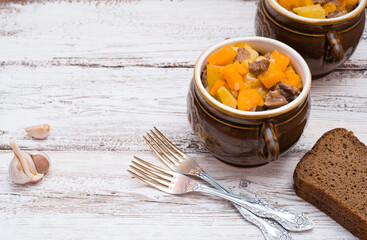 Pumpkin, meat, potatoes and vegetables baked in a ceramic pot on a white wooden table
