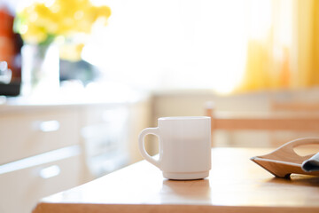 White coffee mug with napkin on table in real kitchen interior with bright natural sunlight