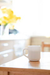 White coffee mug with napkin on table in real kitchen interior with bright natural sunlight