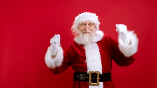 Caucasian Man in Santa Costume Having fun Showing Dance. Concept of New Year and Christmas Holidays. Cheerful Happy Santa Claus is Dancing on Studio Red Background, Waving His Hands Joyfully.