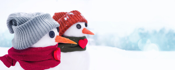Two little cute snowmen in hats and scarves decorated with red hearts in a snow-covered field...