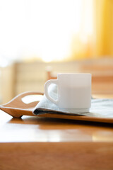 White coffee mug with napkin on table in real kitchen interior with bright natural sunlight