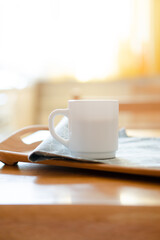 White coffee mug with napkin on table in real kitchen interior with bright natural sunlight