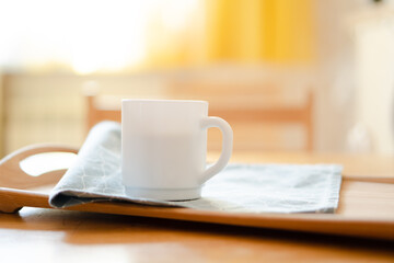 White coffee mug with napkin on table in real kitchen interior with bright natural sunlight