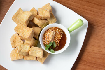 Fried tofu with Thai sweet dipping sauce in a white plate on the wooden floor
